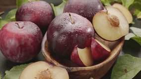 Ripe plums fruits with plum slices slowly move in the wooden bowl on a gray stone table. Nice fruit background for your projects. Macro video shooting.