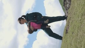 Vertical video. Cheeful young mother hiker with baby carrier enjoying view while hiking in mountains, slow motion. Active travel with family and adventure concept