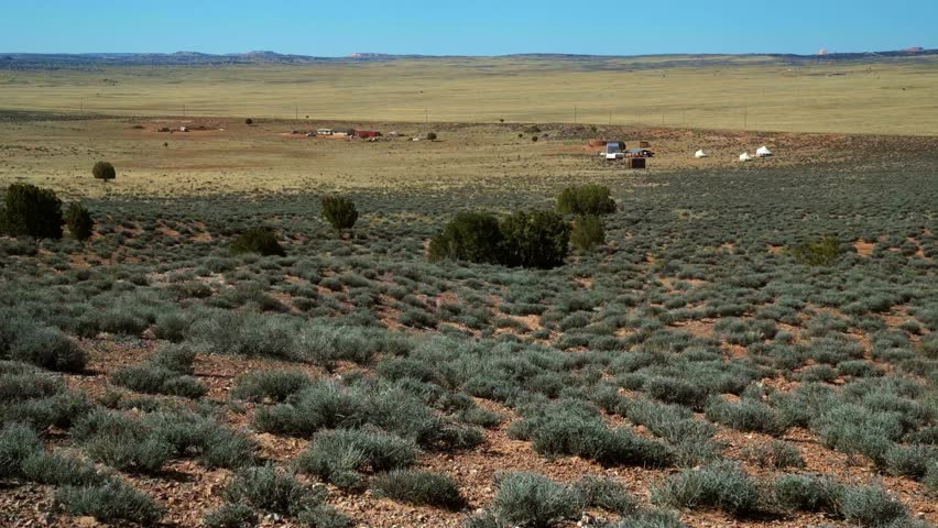 Tilt up extreme wide landscape shot of a large desert plane used for sheep farming with small distant buildings and tents and the ground covered in sage brush in Arizona on a warm sunny spring morning