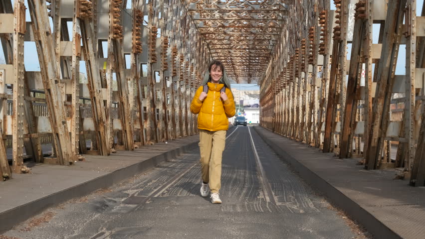 Teen happy walk on old bridge. A view of young girl having joyful promenade on the rusty city bridge during vacation time.