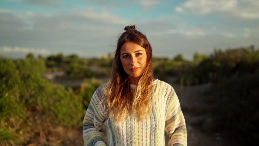 Slow motion dolly toward a model standing and smiling in nature during sunset