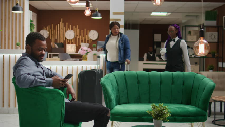 Traveller paying for coffee cup at hotel, using card at pos terminal to buy refreshment from bar. Client thanking employee for serving beverage in lounge area while he waits for check in.