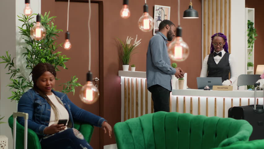 Tourist registering at luxury hotel and receiving room access card, talking to employees about hospitality industry ammenities and services. Receptionist welcoming guest at front desk.