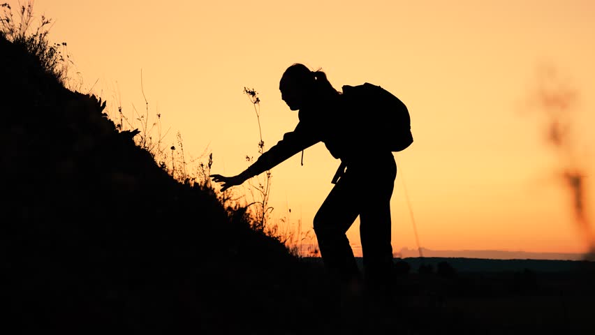 Silhouette of woman with backpack climbing on hill with friend help at sunset. Woman climber gets support from friend on mountain slope. Woman tourist and friend teamwork during difficult climbing Royalty-Free Stock Footage #1109348971