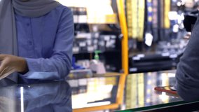 An upwardly mobile Asian Muslim man using a smartwatch to pay for a product at a sale terminal with nfc identification, payment for verification and authentication - Powered by Shutterstock - Get 15% off with code: PIKWIZARD15