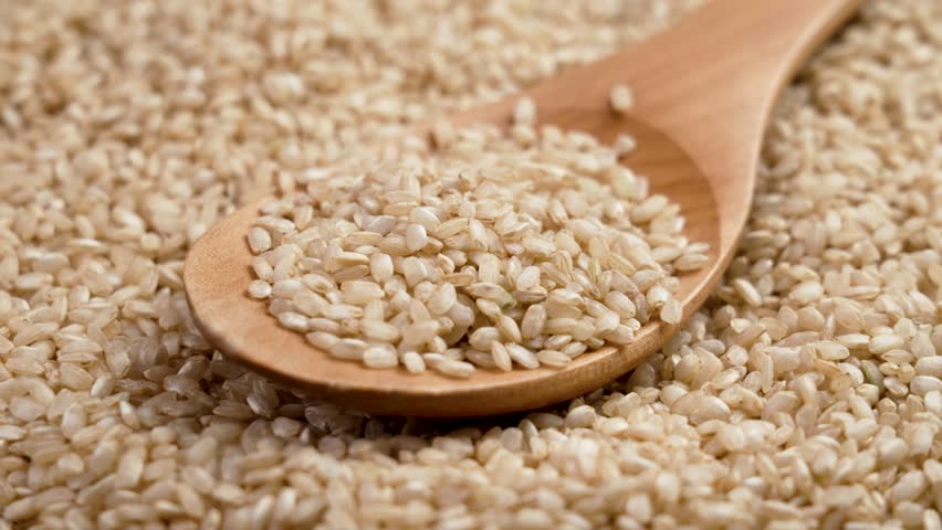 Brown coarse uncooked integral rice in wooden spoon close up. Rotation. Dietary nutritional food