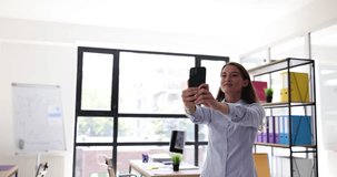Young businesswoman takes selfie on smartphone while spinning smiling in office. Positive emotions and video call