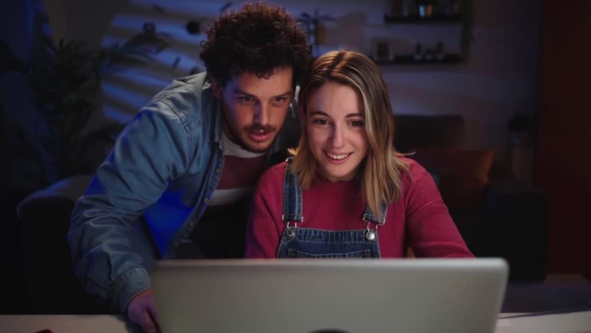 Animated young Caucasian couple looking for bargains on computer in living room at night. Millennial people enjoy online discounts from home using laptop. Positive relationship, sales and black Friday Royalty-Free Stock Footage #1109365329