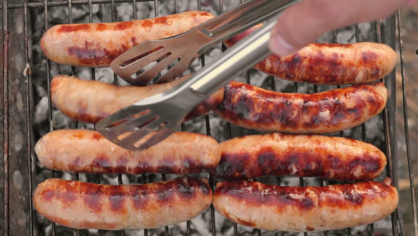 Grilled sausages. Cook man preparing grilling food bbq. Barbecue with smoke, flame outdoors. Tasty juicy german bratwurst. Charcoal kettle grill outside in backyard. Family summer vacation. Close-up Royalty-Free Stock Footage #1109366337