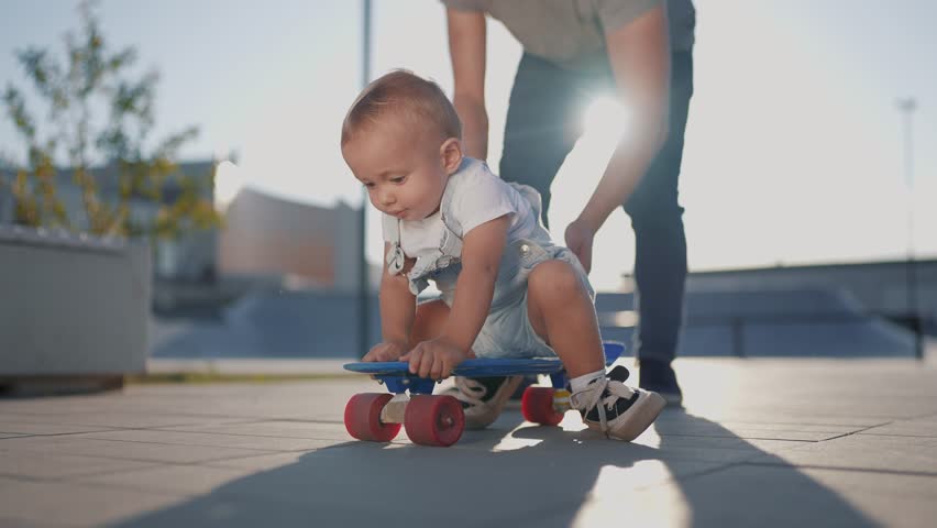 child riding a skateboard along the path. landscape square glare of the sun. child on a skateboard. city landscape. dad rides baby .cheerful child form content lifestyle
