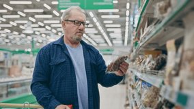 An elderly man in a supermarket stands near the food shelves and compares prices. Pensioner in a grocery shop - Powered by Shutterstock - Get 15% off with code: PIKWIZARD15