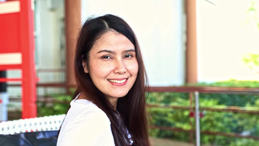 Portrait beautiful asian woman with long, vibrant healthy hair sitting  indoors comfortably, in a good mood, looking at the camera happy.