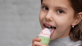 Cute girl enjoys a delicious ice cream cone, outdoors. Child with ice cream on grey background, close-up