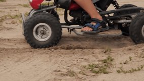 Close-up of ATV wheels kicking up dust and sand on a sharp turn. Slow motion video. A child rushes through the sand on an ATV kicking up dust and dirt. Sand from the road flies from under the wheels.
