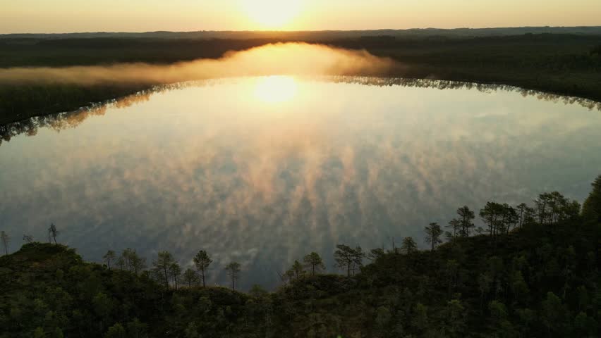 Flying Above the Water and a Sea of Fog at Sunrise. Fog on lake. Golden sunlight rising moving orange mist on water surface in warm summer morning. Misty morning at a foggy lake. Nordic country