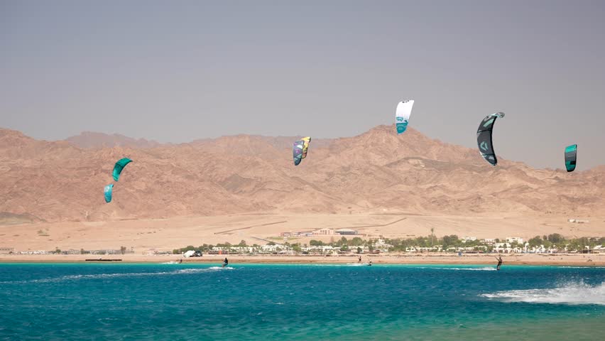 Many kite surfers with colored parafoil wings catching the flow of wind and jumping in Dahab lagoon. Best Kiteboarding Spots Worldwide Royalty-Free Stock Footage #1109376703