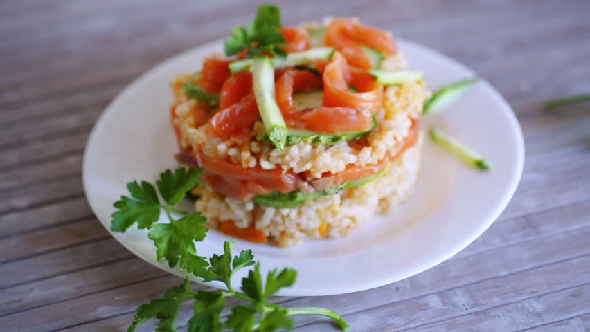 Boiled white rice with salted red fish, cucumbers and other vegetables with herbs in a plate.