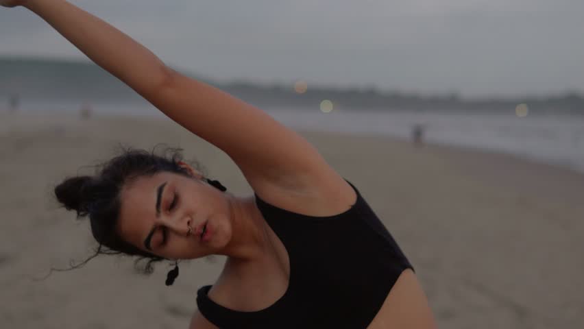 A close-up shot captures an Indian woman focused on her fitness routine at the beach. Her determined expression reflects her dedication to a healthy lifestyle as she exercises by the shore.