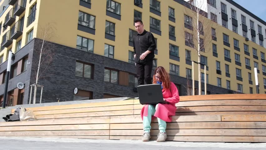 Caucasian man doing somersaults in the street and sits down next to the woman. The guy meets the girl in an unusual way.