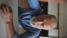 Vertical POV of happy senior elderly 70s man holding smartphone watching mobile video calling online looking at camera sitting at home table. Webcam view of smiling mature aged male talking video chat - Powered by Shutterstock - Get 15% off with code: PIKWIZARD15