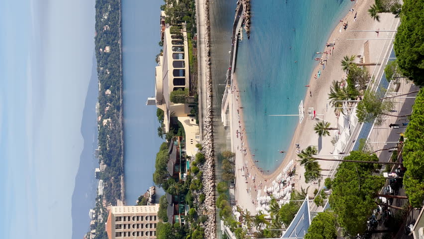 Vertical footage of famous beach of principality of Monaco in sunny day, Italia is on background, new construction, azure water