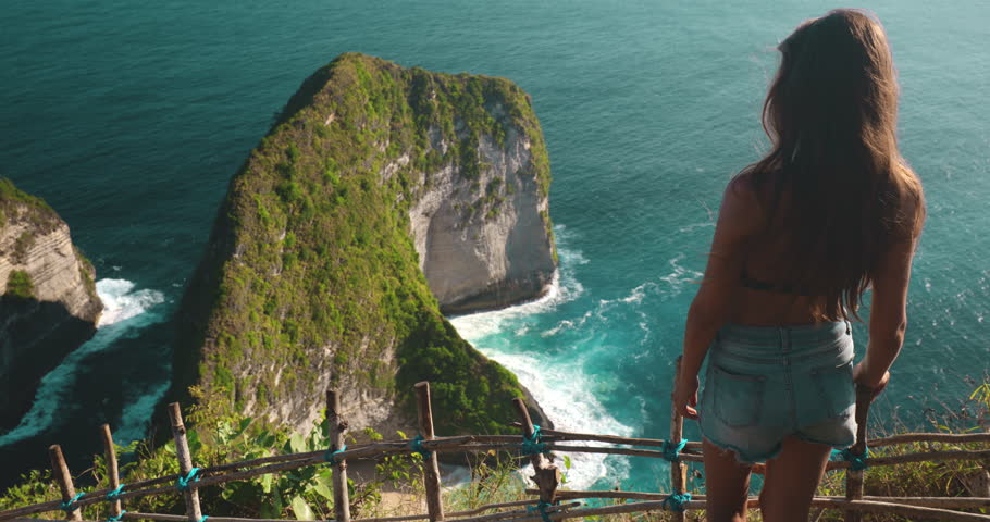 Tourist place to visit - Kelingking Secret Point Beach Indonesia, Nusa Penida Island. Caucasian beautiful woman relax and enjoy aerial ocean mountain wild nature landscape. Slow motion zoom back view Royalty-Free Stock Footage #1109386819