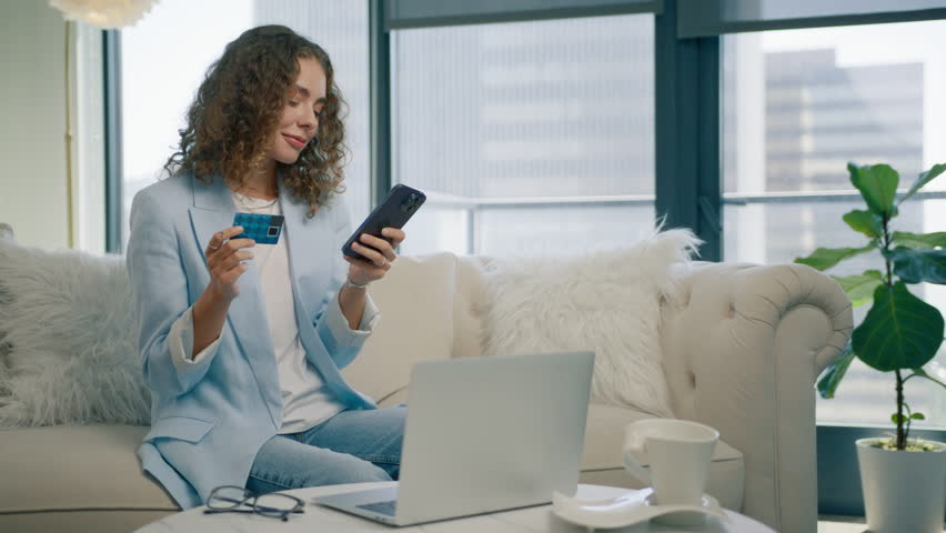 Smiling stylish woman holding smartphone and credit card sitting on couch modern home. Happy female shopper using instant easy mobile payments, customer making purchase in online store, e banking app Royalty-Free Stock Footage #1109388313