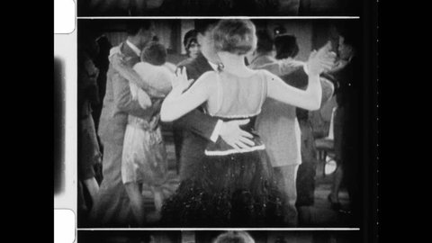 1920s United States. Close up of flappers legs as she performs the steps to The Charleston. Man and woman party and dance cheek to cheek in nightclub speakeasy. 4K Overscan vintage archival film संपादकीय स्टॉक व्हिडिओ