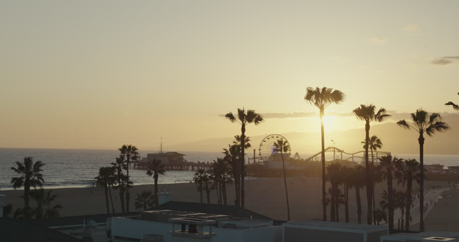 Beautiful Sunset View Over Santa Monica Pier in Los Angeles, the United States of America. California Beach and Amusement Park Landmark with Palm Trees, Ocean, People Walking by the Shore