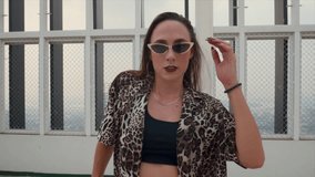 A medium close-up shot of a stylish woman wearing sunglasses and leopard print shirt, showcases her dance skills energetically on a rooftop - Powered by Shutterstock - Get 15% off with code: PIKWIZARD15