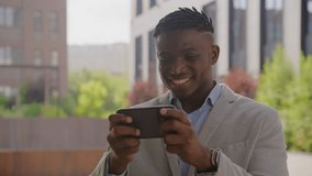 Businessman Playing Video Game Application on Cellphone. Black man wins using smartphone sitting outside.