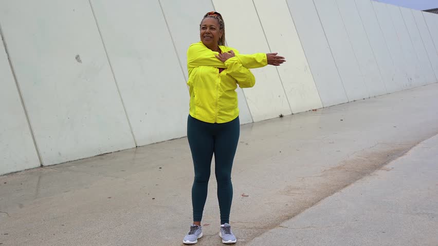 Fit african senior woman doing sport stretching workout during rainy day in the city