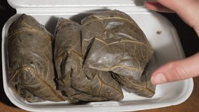 This close up video shows a hand grabbing dim sum lotus leaf wrapped sticky rice from a carry out box.