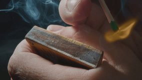 Hands lights a match with a green sulfur head, slow motion. Strikes a match on the side of the box. Smoke and fire appear. The flame ignites. The match lights up, burns and goes out. Super macro shot - Powered by Shutterstock - Get 15% off with code: PIKWIZARD15