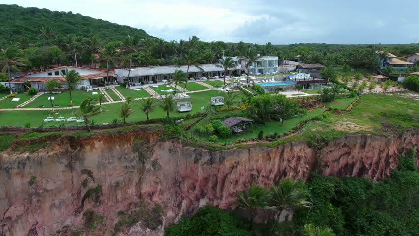Aerial Panning Shot Of Tourist Resort Amidst Green Plants And Trees On Cliff Against Sky - Pipa Beach, Brazil