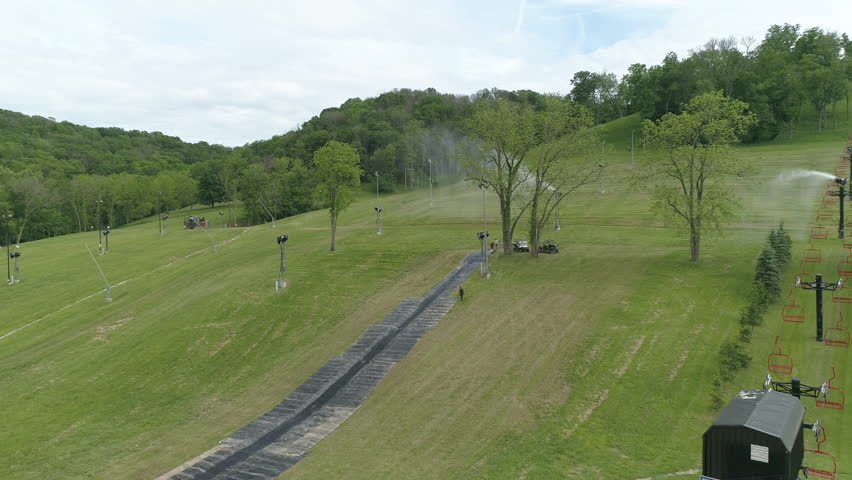 Aerial Forward Shot Of People And Sprinklers On Green Grass Over Hill Against Sky - Crawfordsville, Indiana