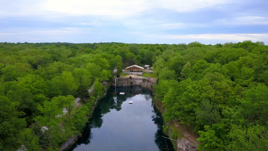 Aerial Descending Backward Shot Of People In Pond With Floating Platforms Amidst Trees And Plants Against Sky - Crawfordsville, Indiana