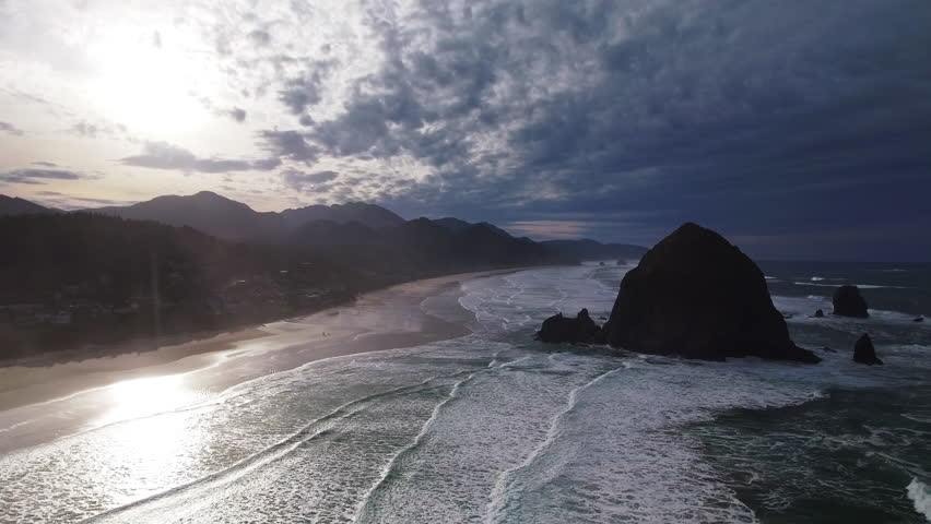 Aerial Panning Shot Of Waves In Sea With Rock Formation Near Mountains Against Sky During Sunset - Portland, Oregon