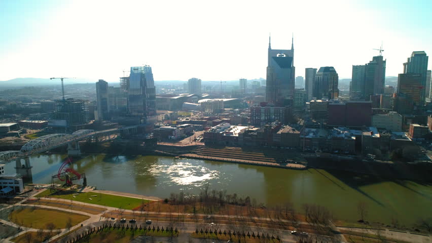 Aerial Forward Shot Of Cumberland River With Bridge Near Buildings In City Against Sky - Nashville, Tennessee