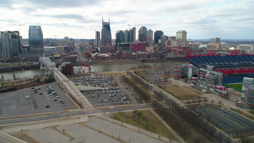 Aerial Descending Forward Over Cars Near Nissan Stadium And River In City Against Cloudy Sky - Nashville, Tennessee