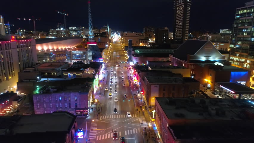 Aerial Backward Shot Of People And Cars On Streets Amidst Buildings In City At Night - Nashville, Tennessee
