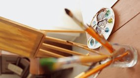 a color palette with paints on a wooden table, in the foreground is a blurred female hand that selects and pulls an artist's bone from a cup. vertical video. close-up - Powered by Shutterstock - Get 15% off with code: PIKWIZARD15