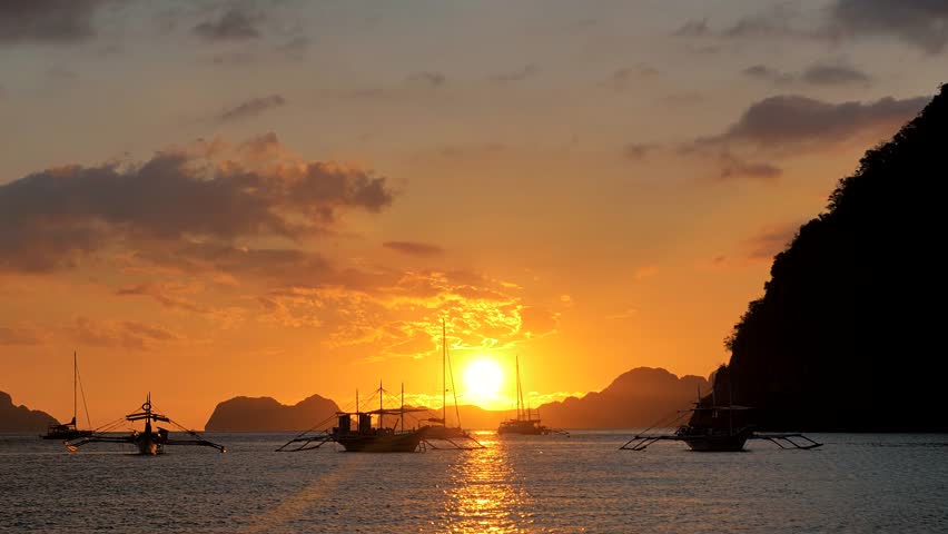 Traditional philippine boat bangka at sunset time. Beautiful sunset with silhouettes of philippine boats in El Nido, Palawan island, Philippines. Orange sky sunset paradise beach. Royalty-Free Stock Footage #1109418441