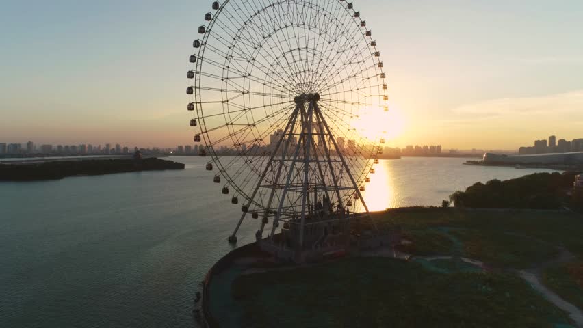 Aerial cityscape of a ferris wheel, boats and skyline in the sunset on Jingji lake, Suzhou, China. Camera moves up forward