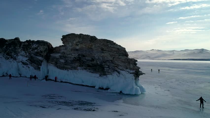 Aerial view on the rocky ice covered island in lake Baikal. Groups of tourist walking around on the cracked ice. Famous tourist spot. Beautiful winter landscape of lake Baikal