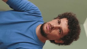 Vertical video, Young man with curly hair and beard using laptop at home in cozy living room