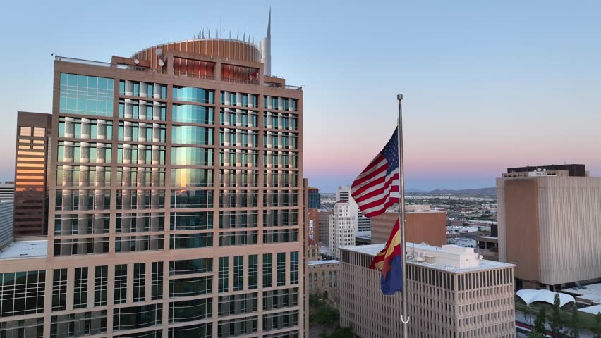 Phoenix City hall skyscraper with America and Arizona flags waving in downtown Phoenix, AZ. Aerial shot of flags and skyscrapers during beautiful sunset.