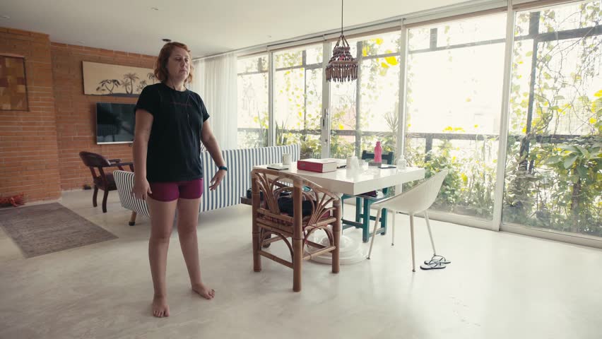 Young woman doing squats to lose weight in the bright living room of her home