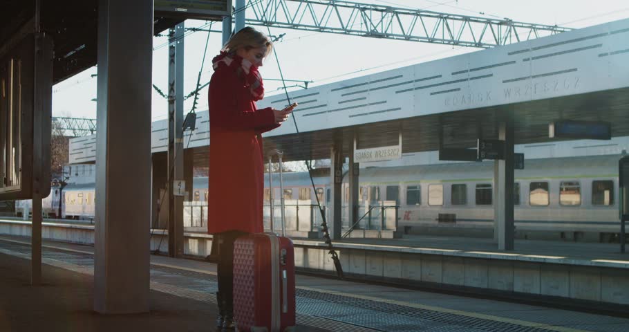 Portrait of Young Blonde Woman Typing on a Mobile Phone Outdoors. Girl Stands on the Train Platform and Looks at her Phone, Scrolling Through Social Networks or Looking at the Train Schedule Online.