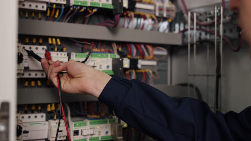 Tests wiring, Safety protocols, Industrial wiring. At manufacturing facility, electrician measures electrical current in control panel using multimeter. Royalty-Free Stock Footage #1109429959